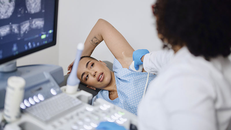 Médica fazendo exame de ultrassom de mama em paciente deitada