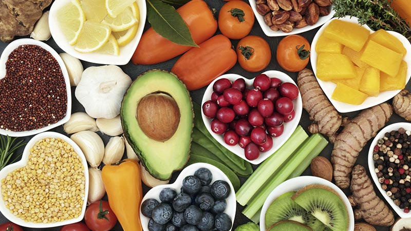 Vários alimentos saudáveis, como abacate, mirtilo e verduras, em cima de uma mesa