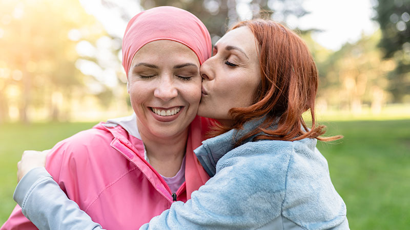 Mulheres abraçando com os olhos fechados enquanto beijam o lutando contra o câncer