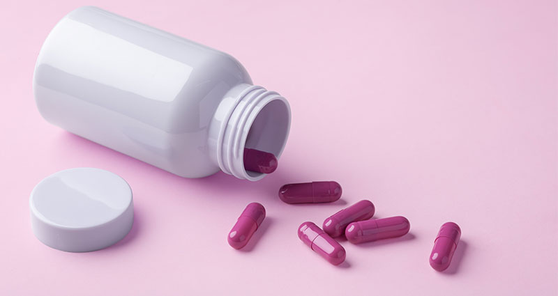 Cápsulas de pílula derramando para fora do frasco no fundo rosa pastel
