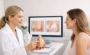 Profissional de saúde conversando com paciente, mostrando modelo anatômico e imagens em computador sobre cirurgia.